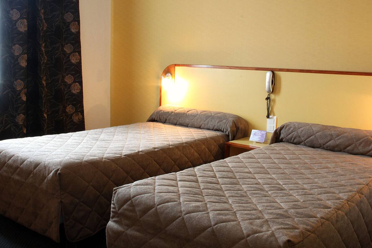 A hotel room with two single beds, a bedside table with a lamp, and a telephone.