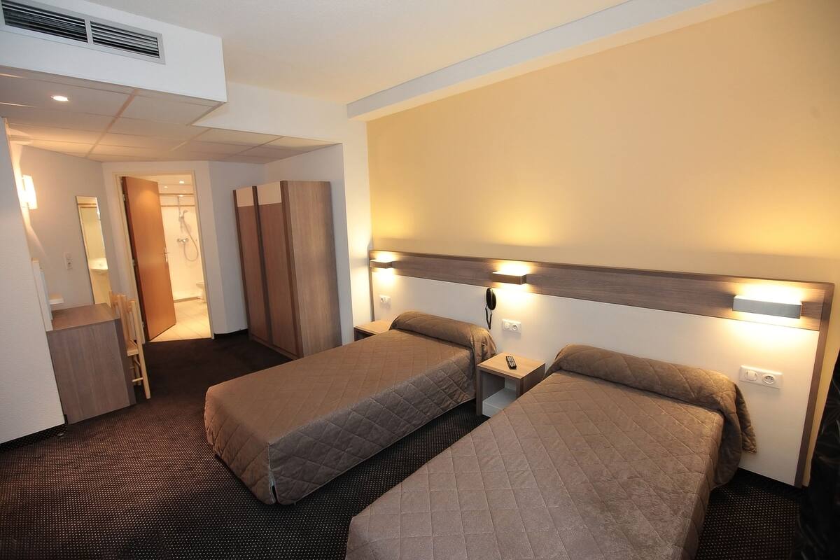 A hotel room with two beds, a desk, a chair, and a wardrobe.