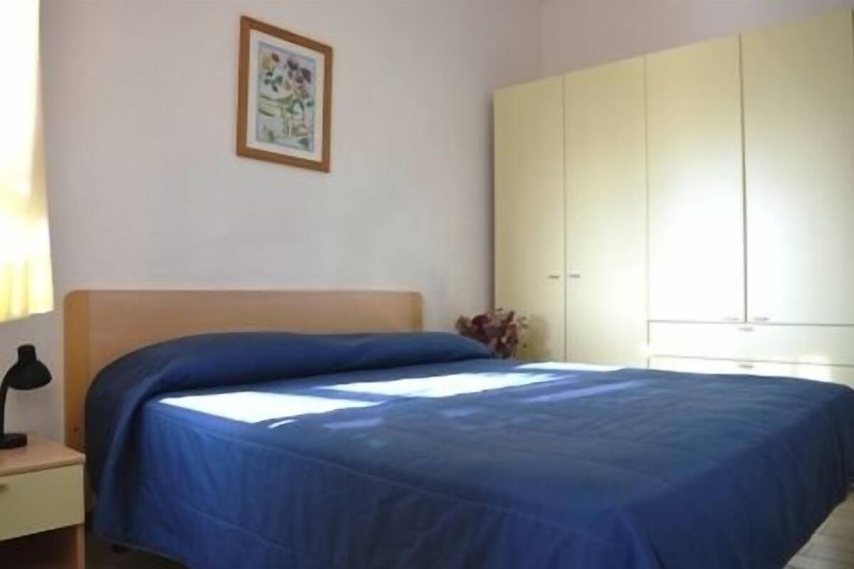 A bedroom with a bed, a nightstand, a wardrobe, and a framed picture on the wall.