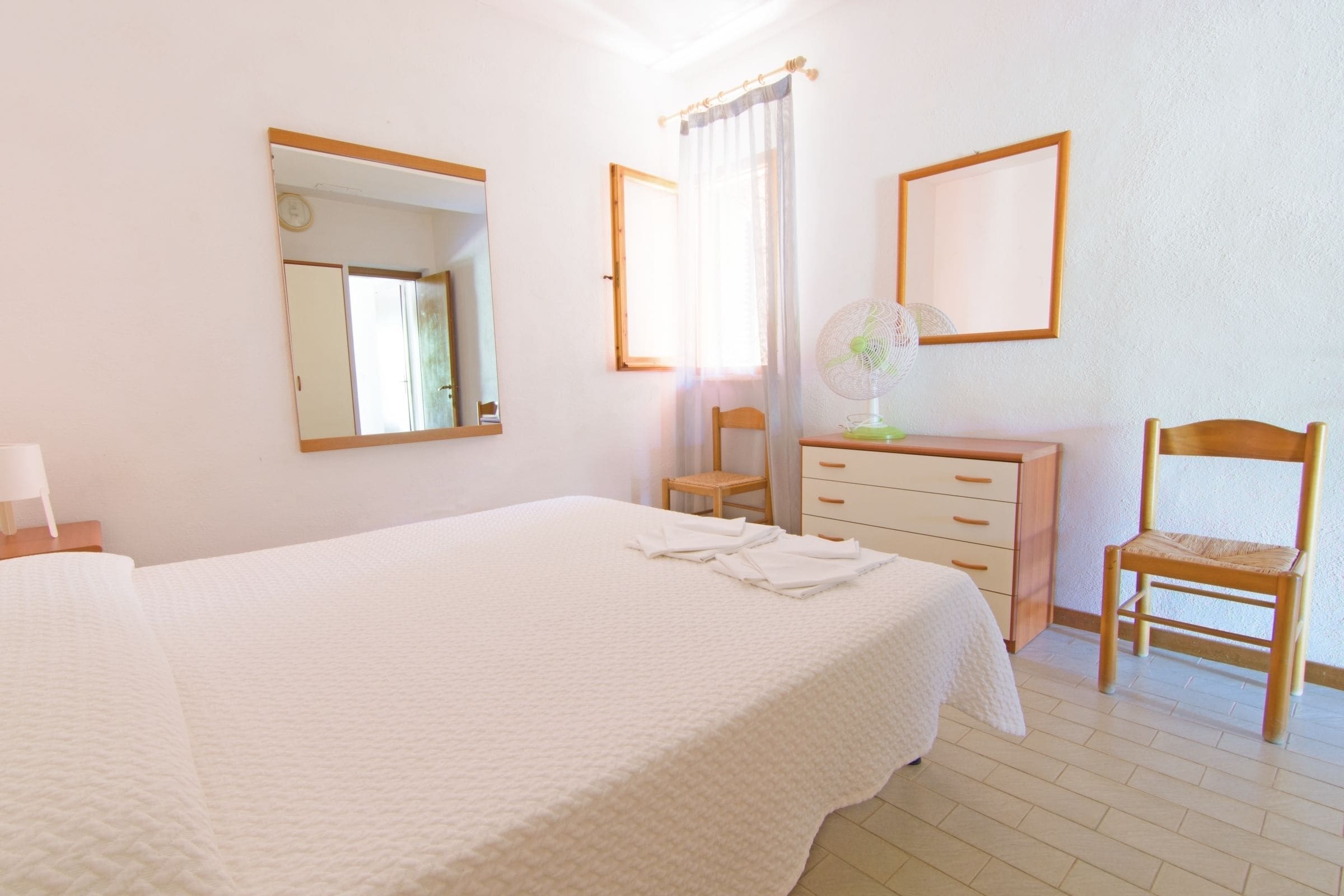 A bedroom with a bed, a dresser, a chair, a mirror, and a window with curtains.
