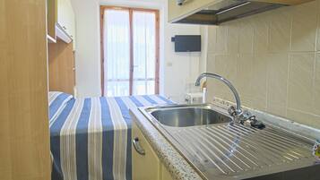Una cocina compacta con un lavamanos, una ventana con cortinas y una puerta que da a otra habitación.