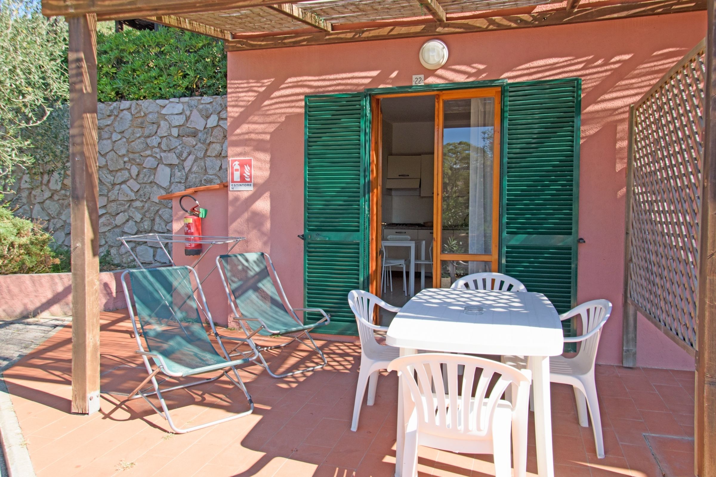 An outdoor patio with a table and chairs, a fire extinguisher, and a stone wall.