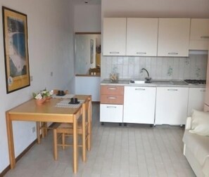 Une cuisine compacte avec des meubles blancs, une table à manger en bois et un petit plan de travail.