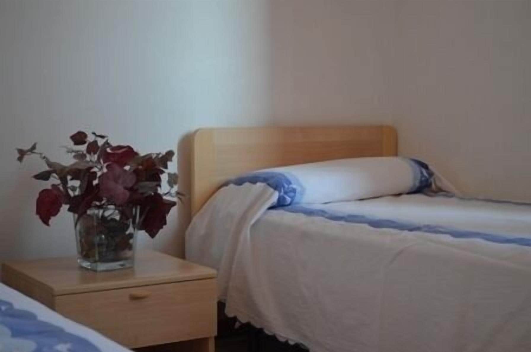 Un dormitorio con una cama individual, una mesita de noche y un florero con flores secas.