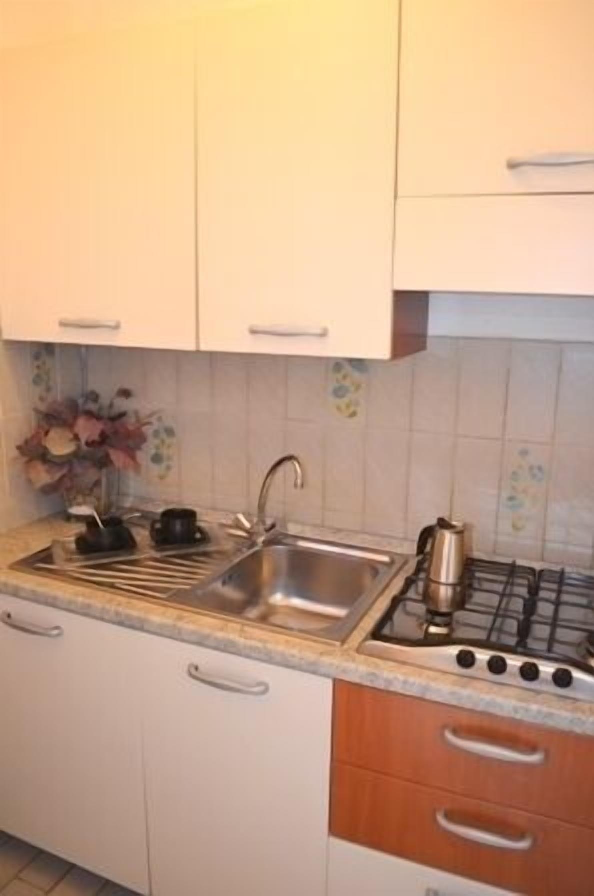 A kitchen with white cabinets, a stainless steel sink, a stove, and a countertop with a kettle and teapot.