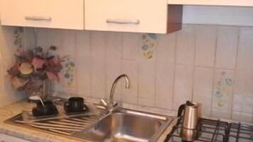 A kitchen with white cabinets, a stainless steel sink, a stove, and a countertop with a kettle and teapot.