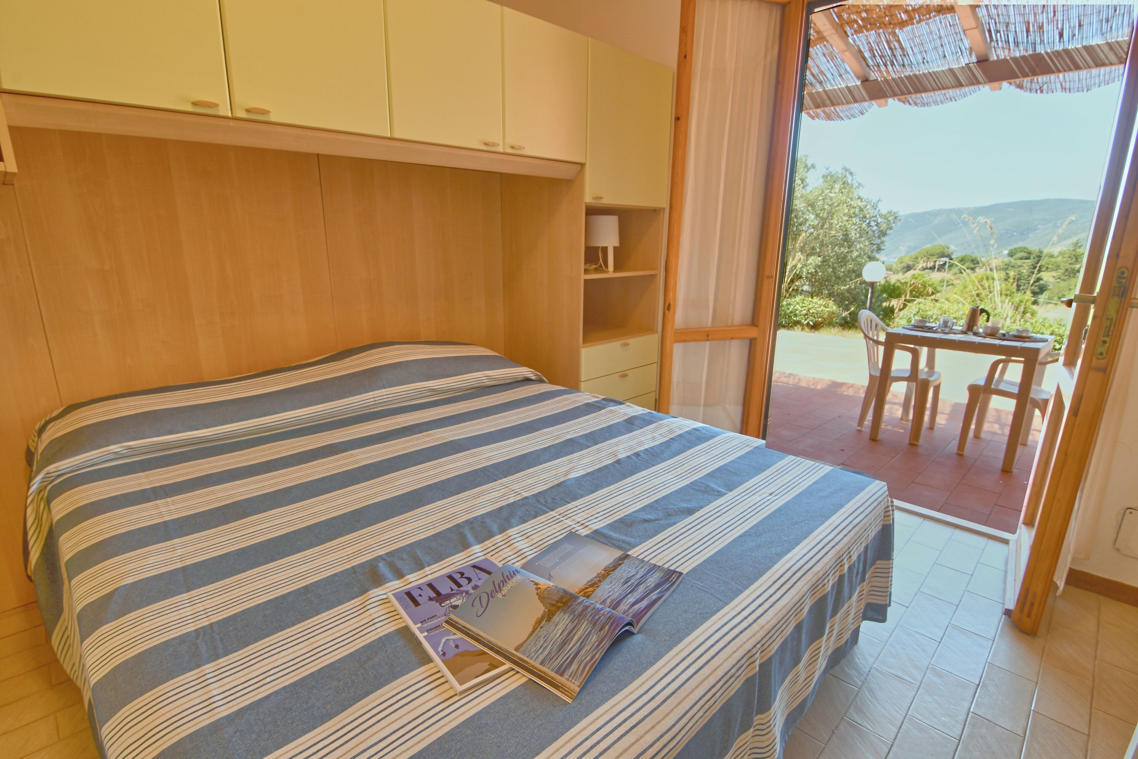 A bedroom with a bed, a table, and chairs outside the window.
