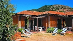 A building with a tiled roof, outdoor seating area with chairs, and a view of a mountainous landscape. - Appartamenti Elbamar Lacona (Capoliveri)