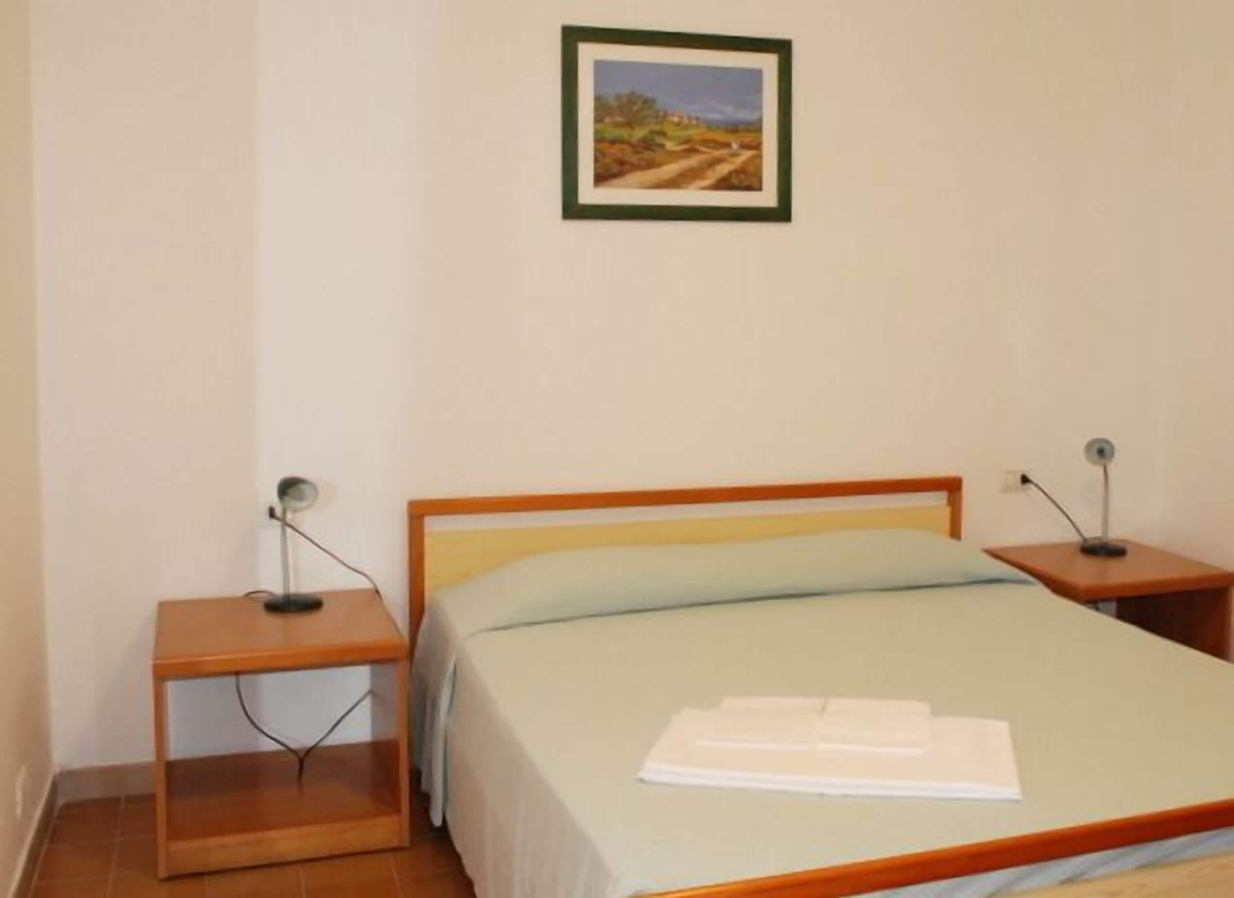 A simple room with a bed, two bedside tables, and a framed picture on the wall.
