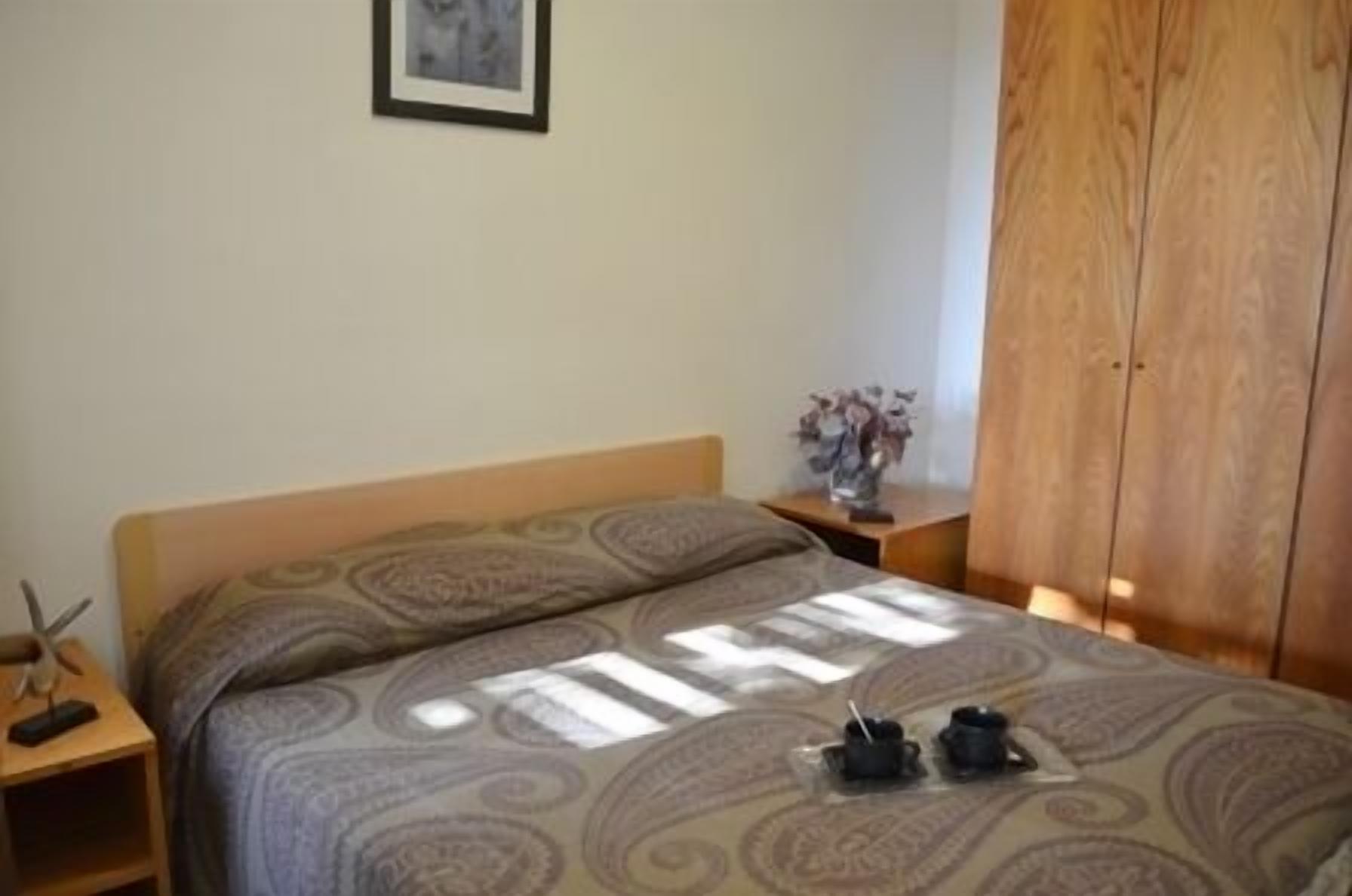 Ein Schlafzimmer mit Bett, Nachttisch, Holzschrank und einem gerahmten Bild an der Wand.