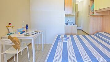 A small, compact room with a bed, a table with chairs, a sink, and a fan.