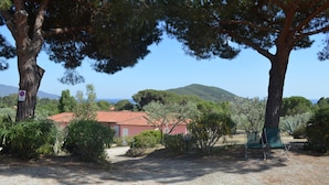 A rural setting with a red-roofed building, surrounded by trees and shrubs, with a clear view of the hills in the background. - Appartamenti Elbamar Lacona (Capoliveri)