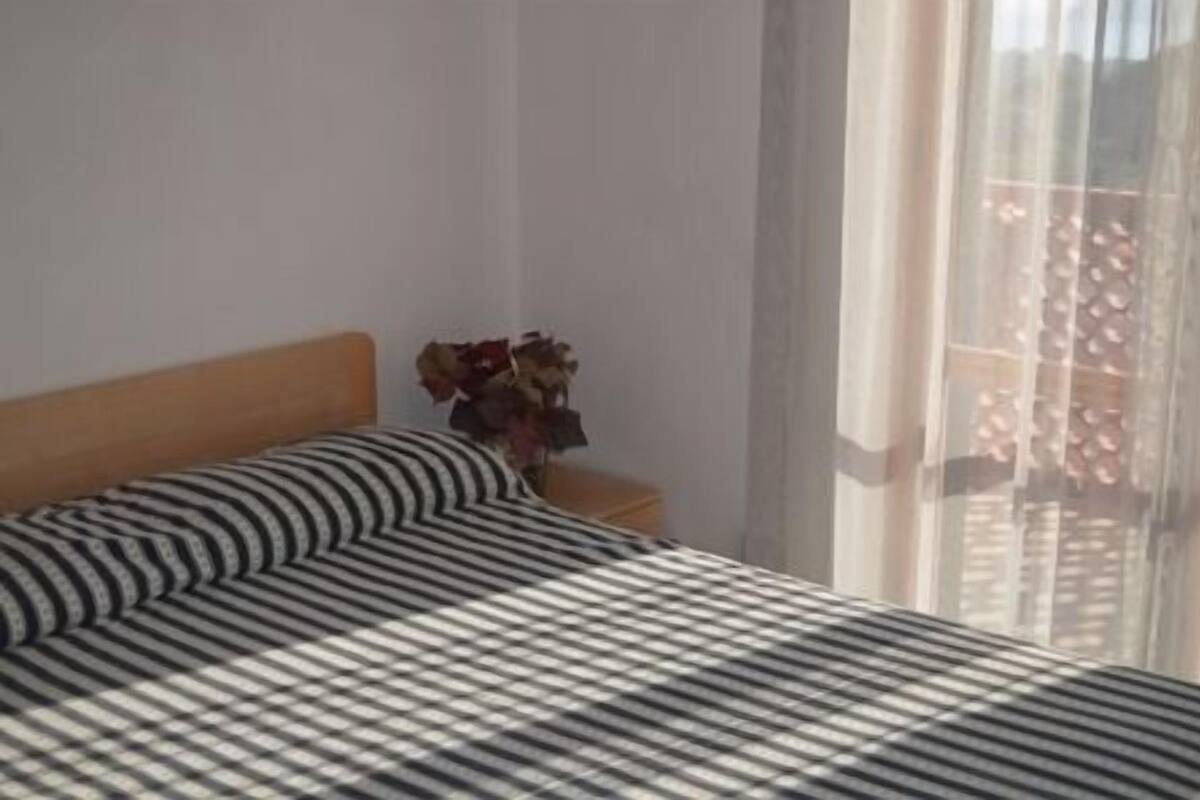 A bed with striped bedding, a wooden headboard, and a vase with dried flowers on a nightstand.