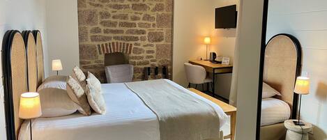 A hotel room with a large bed, a desk, a chair, a television, and a stone wall.
