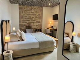 Una habitación de hotel con una cama grande, un escritorio, una silla, un televisor y una pared de piedra.