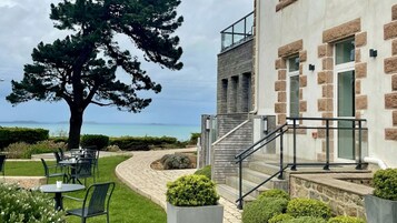 A building with a stone facade, a staircase, and outdoor seating with a view of the sea.