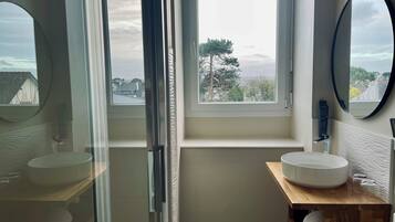 A modern bathroom with a large window, a round mirror, and a wooden vanity.