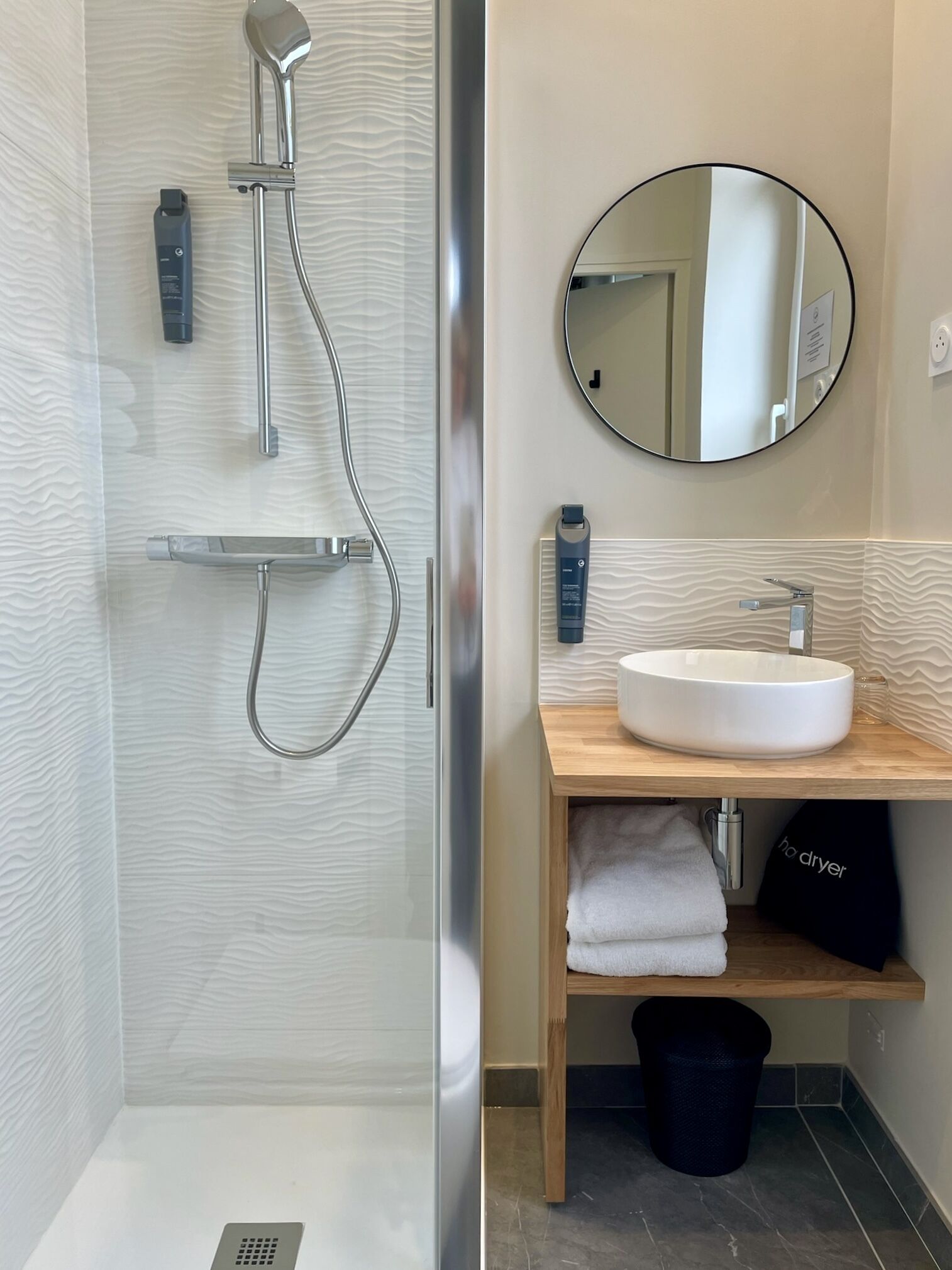 Une salle de bain moderne avec une douche à parois de verre, un meuble-lavabo en bois avec un miroir rond et un lavabo blanc.