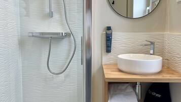 Une salle de bain moderne avec une douche à parois de verre, un meuble-lavabo en bois avec un miroir rond et un lavabo blanc.