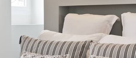 Une chambre à coucher avec un lit, des oreillers, une fenêtre et un miroir.