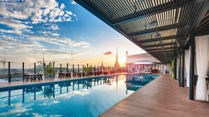 A swimming pool with a wooden deck, outdoor seating, and a view of a temple in the background. - NagaWorld Hotel & Entertainment Complex (Phnom Penh)