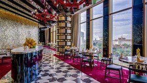A modern restaurant with a patterned floor, a central bar, and large windows offering a city view. - NagaWorld Hotel & Entertainment Complex (Phnom Penh)