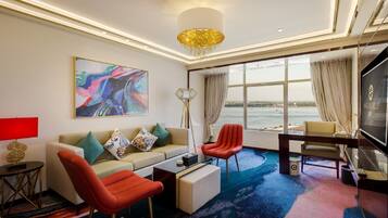 A modern hotel room with a large window, a sofa, a red chair, a coffee table, and a TV.