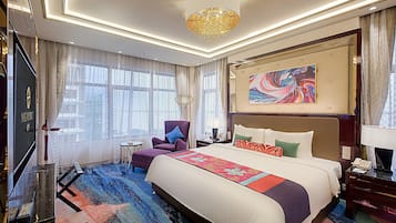 A hotel room with a large bed, a chandelier, a painting, and a view of the city through large windows.