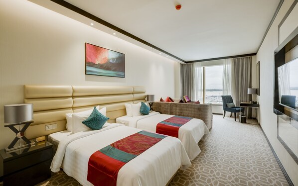 Une chambre d’hôtel avec deux lits, un bureau, une chaise, une grande fenêtre donnant sur un beau paysage et un tableau au mur.