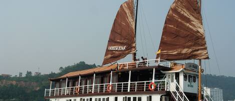 A large boat with two large sails, a deck with railings, and lifebuoys.