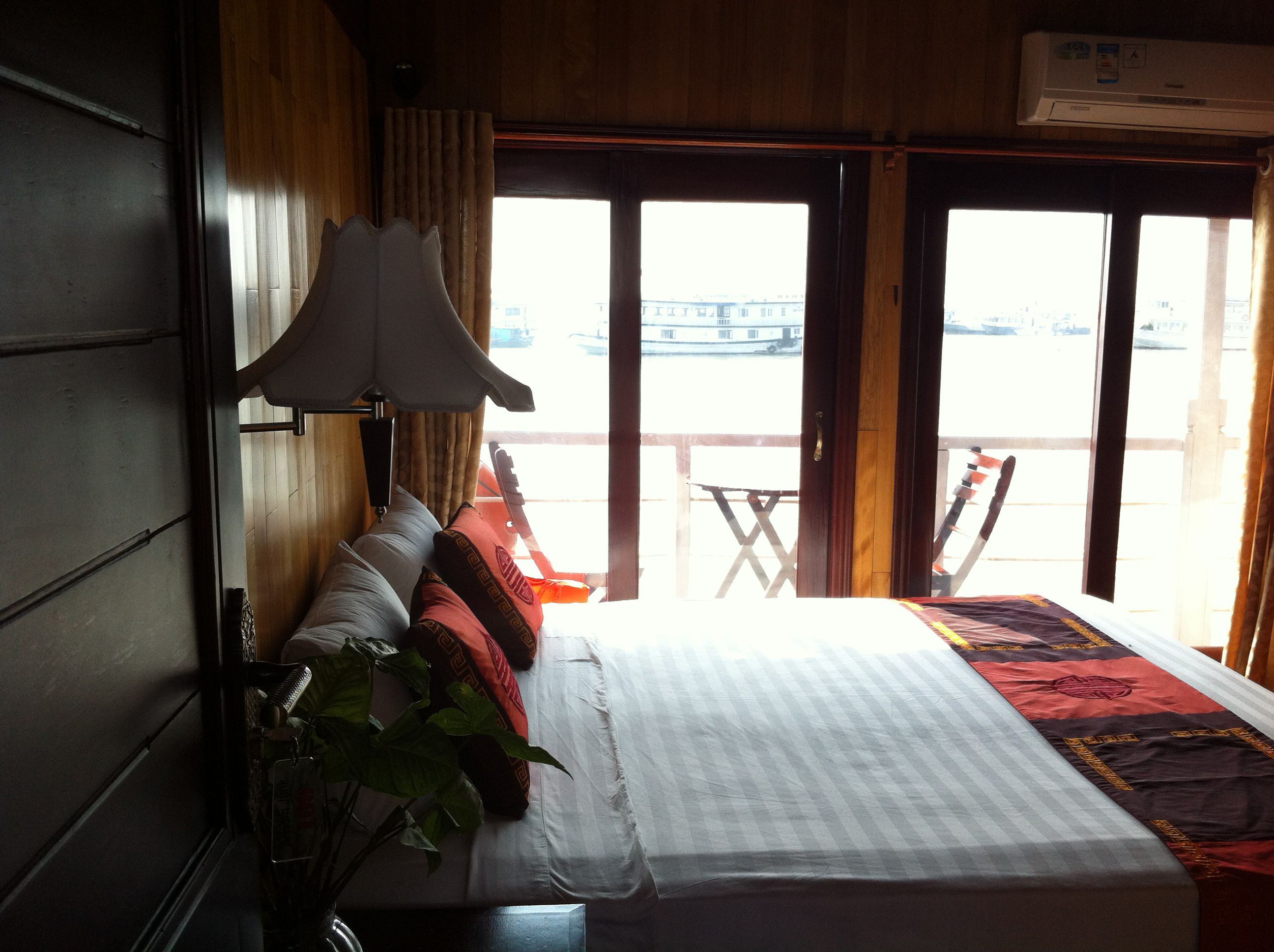 Ein Hotelzimmer mit Bett, Lampe, Pflanze und Blick ins Freie.
