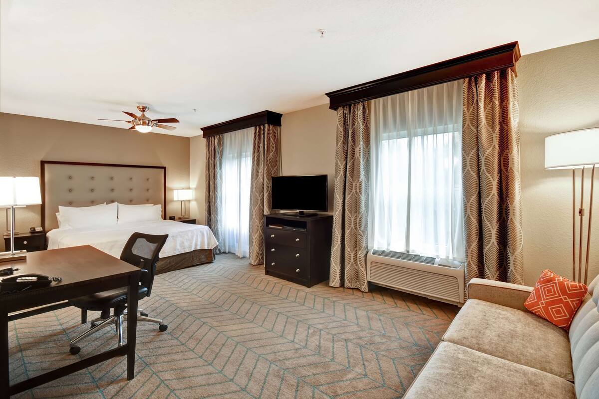 A hotel room with a bed, desk, chair, television, and a sofa.