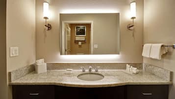 A bathroom with a granite countertop, a sink, two towel racks, and a mirror.
