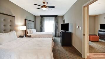 A hotel room with two beds, a ceiling fan, a TV, and a desk.