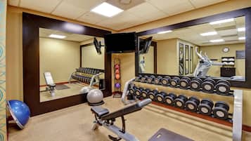 Un gimnasio con equipo de ejercicio, una banca y una pared llena de mancuernas.