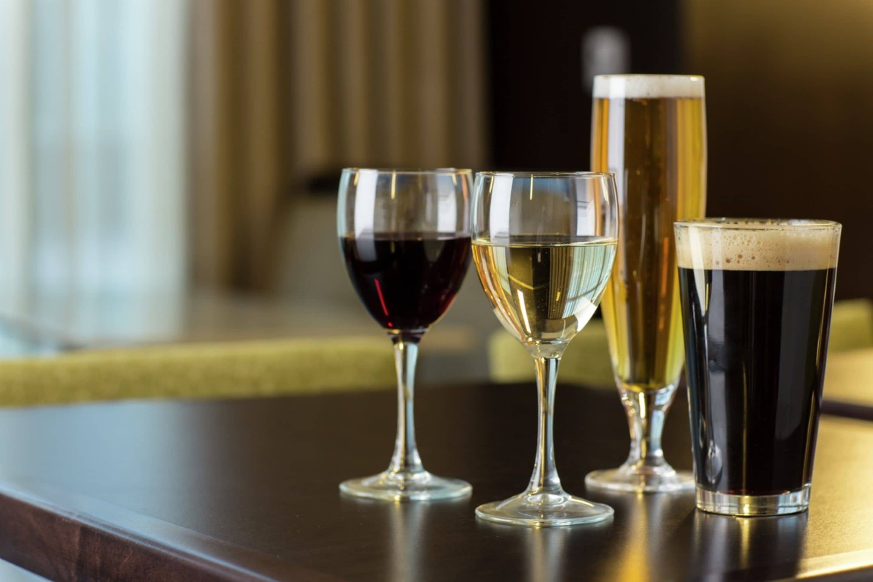 Four glasses of different beverages on a wooden table.