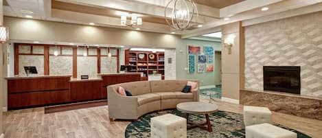 A hotel lobby with a reception desk, a curved sofa, two ottomans, a round coffee table, and a fireplace.