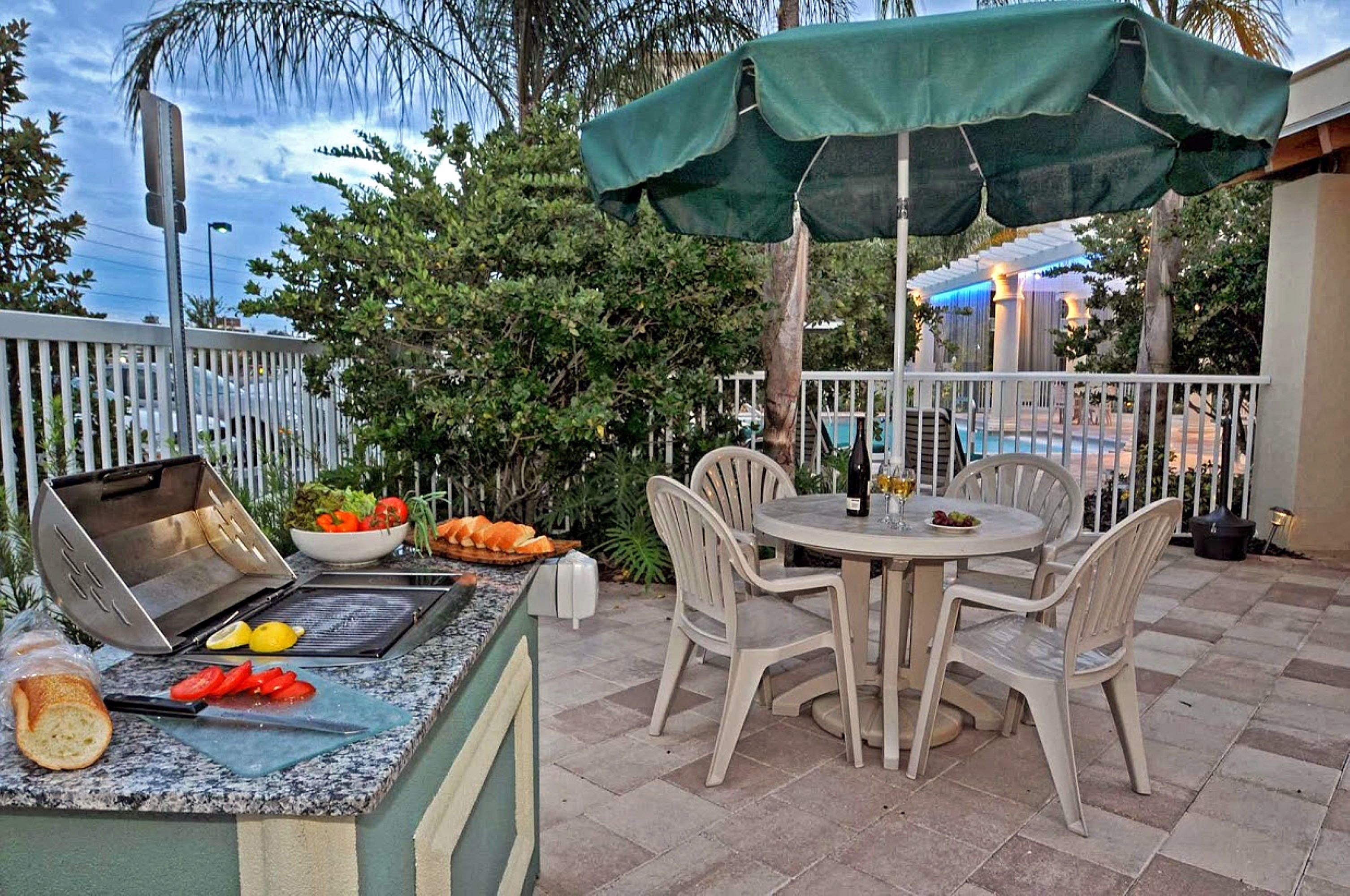Un patio al aire libre con una parrilla, mesa de comedor, sillas y una piscina al fondo.