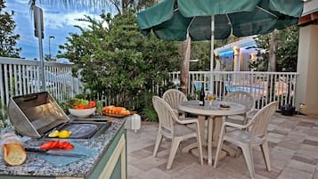 Un patio al aire libre con una parrilla, mesa de comedor, sillas y una piscina al fondo.