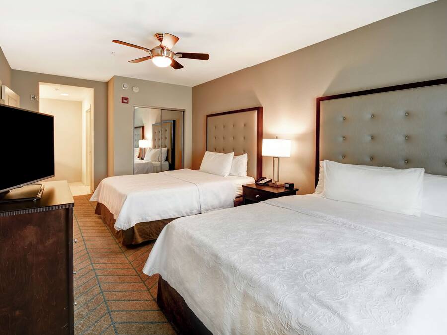 A hotel room with two beds, a television, a ceiling fan, and a mirror.