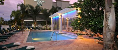 Un espace piscine d’hôtel comprenant des chaises longues, une piscine et un espace de repos abrité.