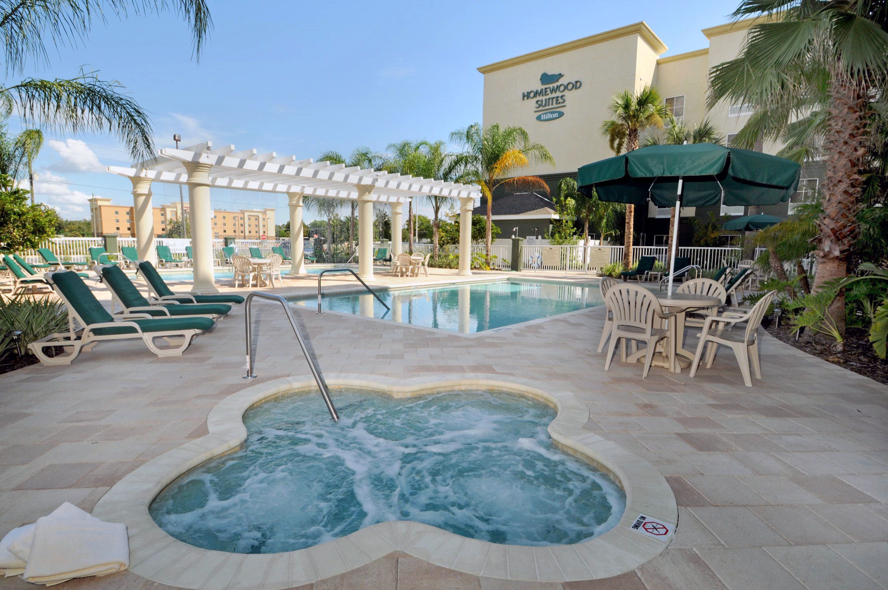 A hotel pool area with lounge chairs, a hot tub, and umbrellas.