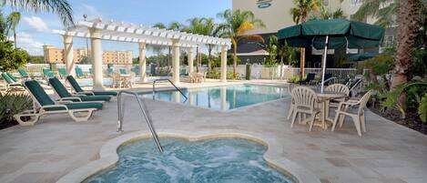 A hotel pool area with lounge chairs, a hot tub, and umbrellas.