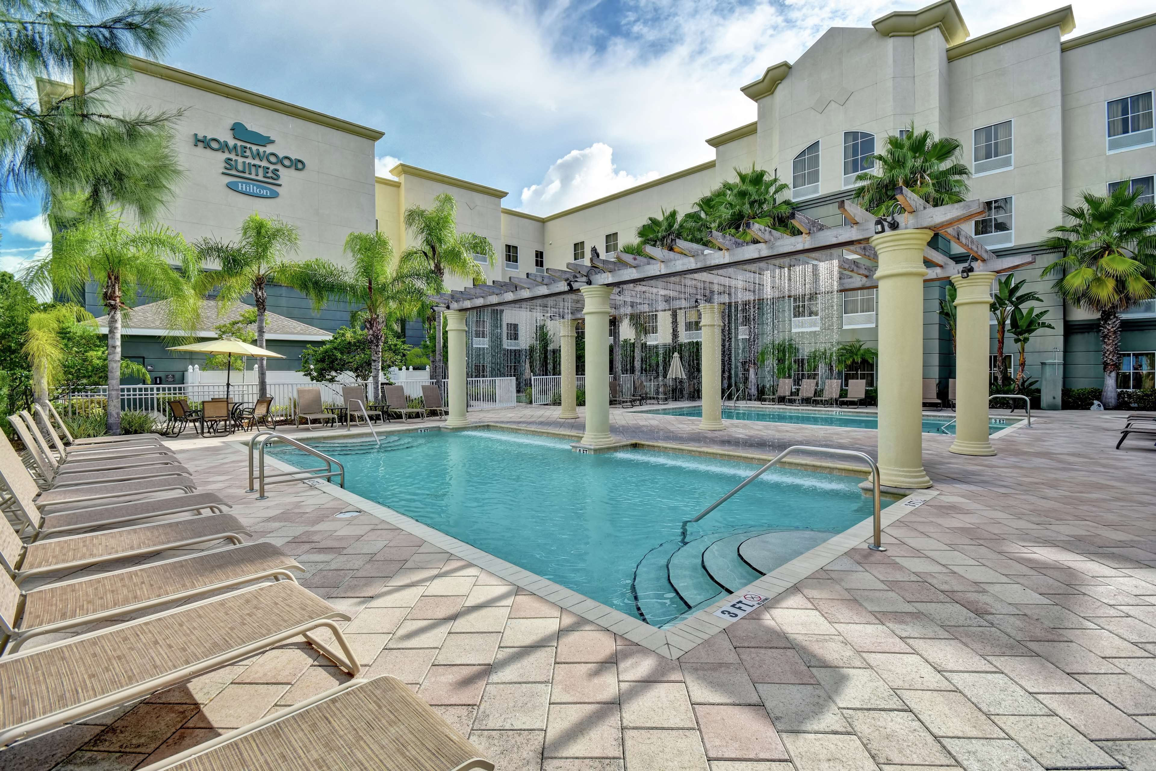 A hotel pool area with lounge chairs, a pergola, and palm trees.