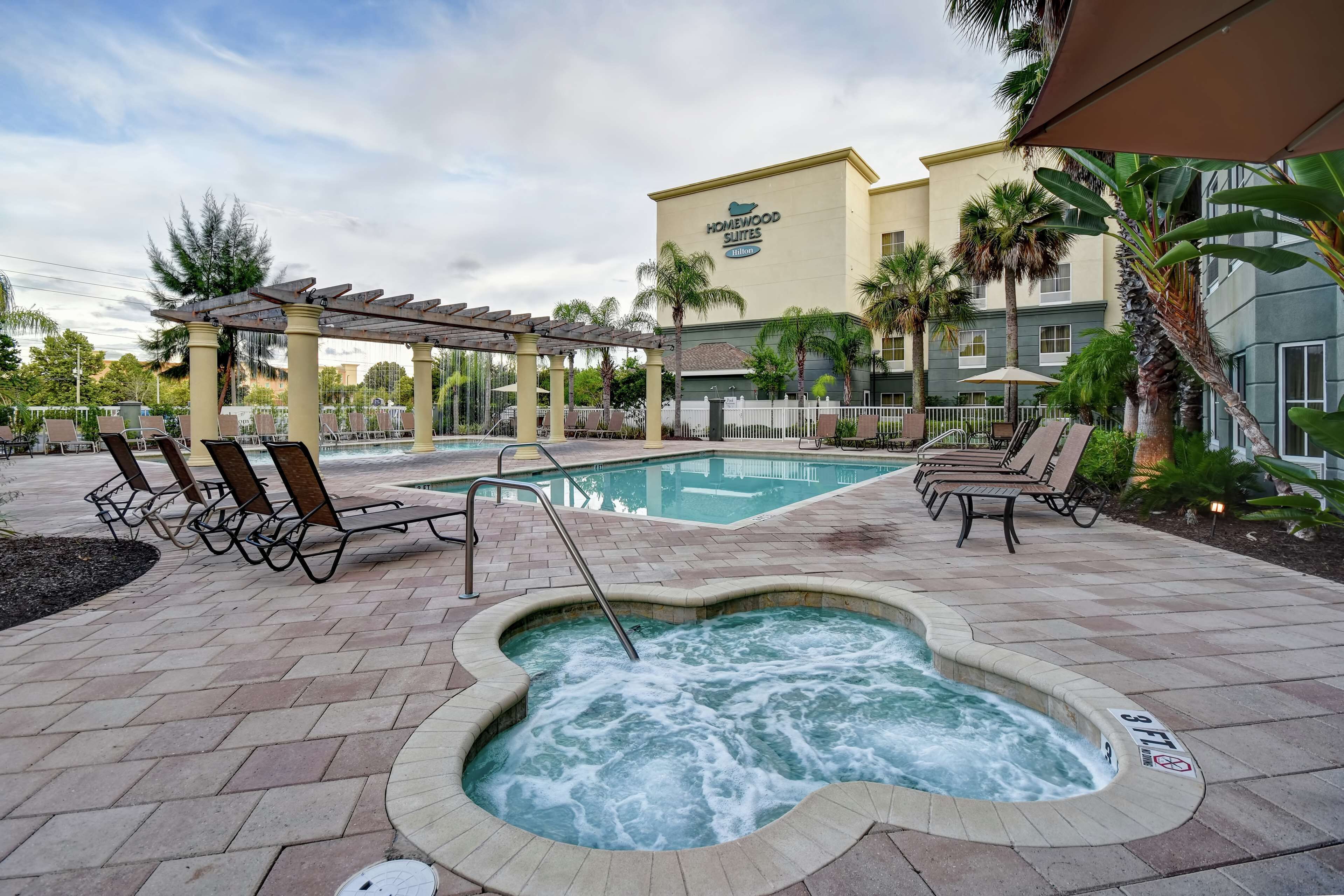 A hotel pool area with lounge chairs, a hot tub, and a covered seating area.