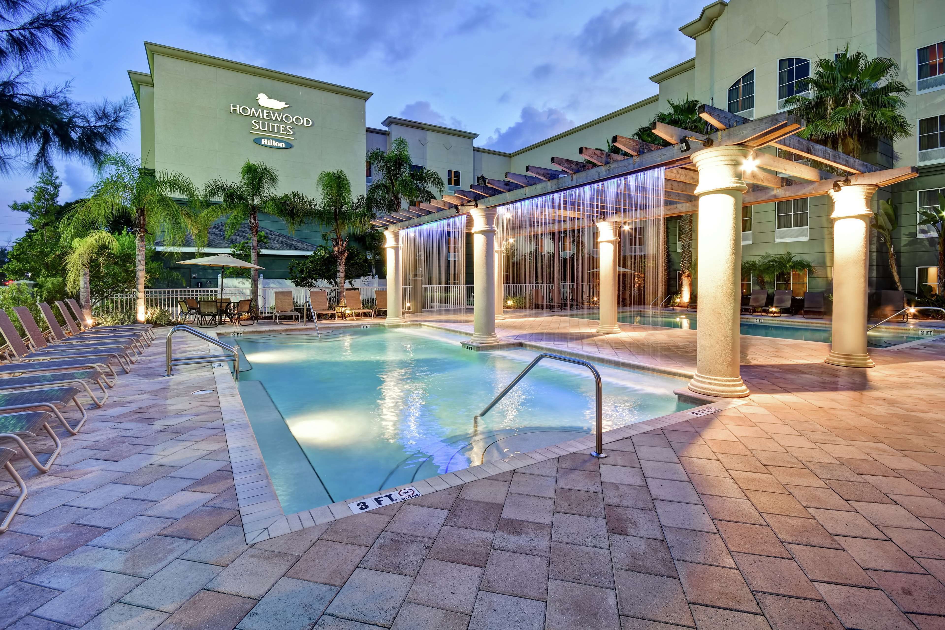 A hotel pool area with a clear pool, lounge chairs, and a covered seating area.
