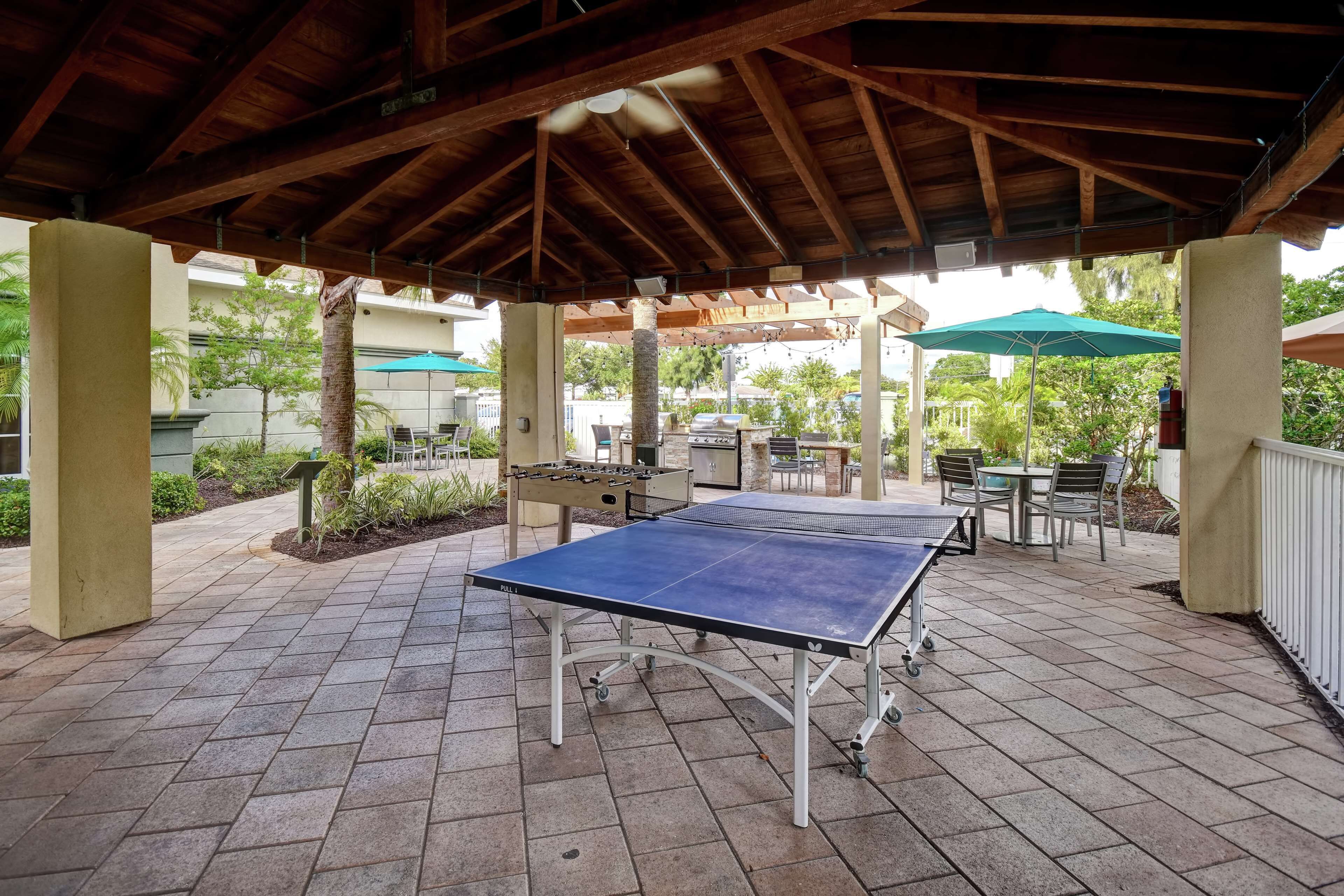 An outdoor patio with a ping pong table, seating area, and barbecue setup.