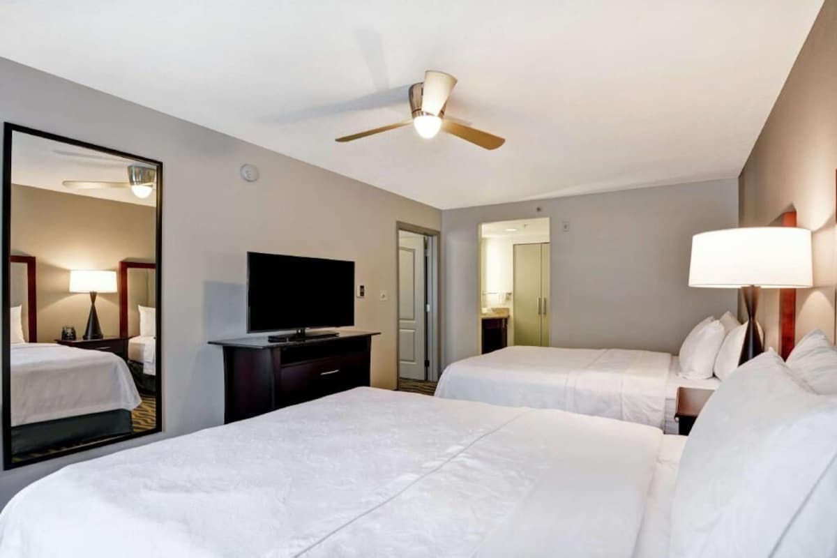 Quarto de hotel com duas camas, televisão, ventoinha no teto e um espelho grande.