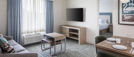 Ett hotellrum med en säng, ett skrivbord, en tv, ett matbord med stolar och en soffa.