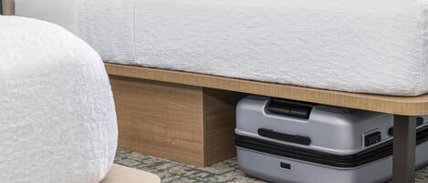 A bed with a white mattress, a wooden headboard, and a suitcase under the bed.
